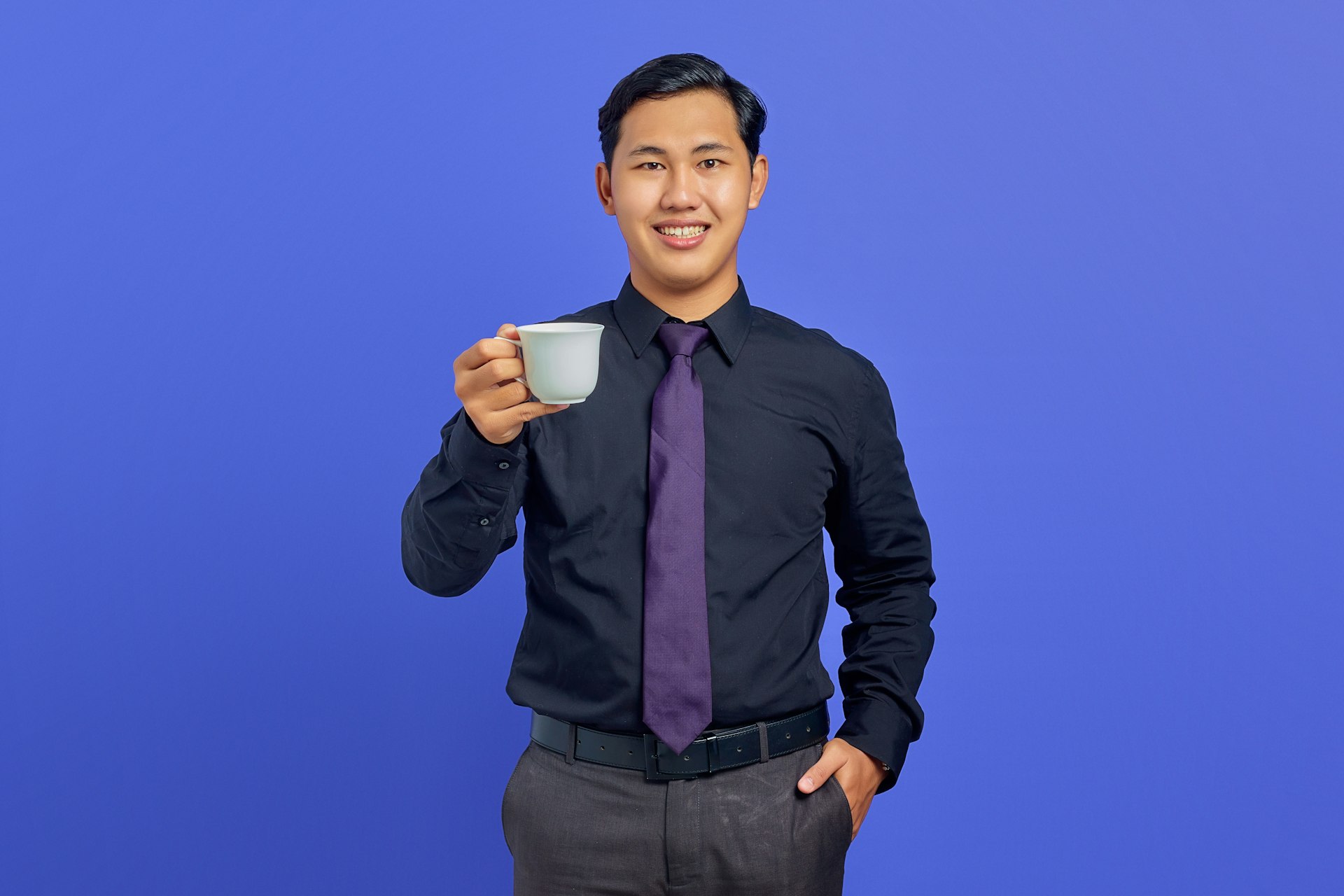 a man in a black shirt and tie holding a cup of coffee